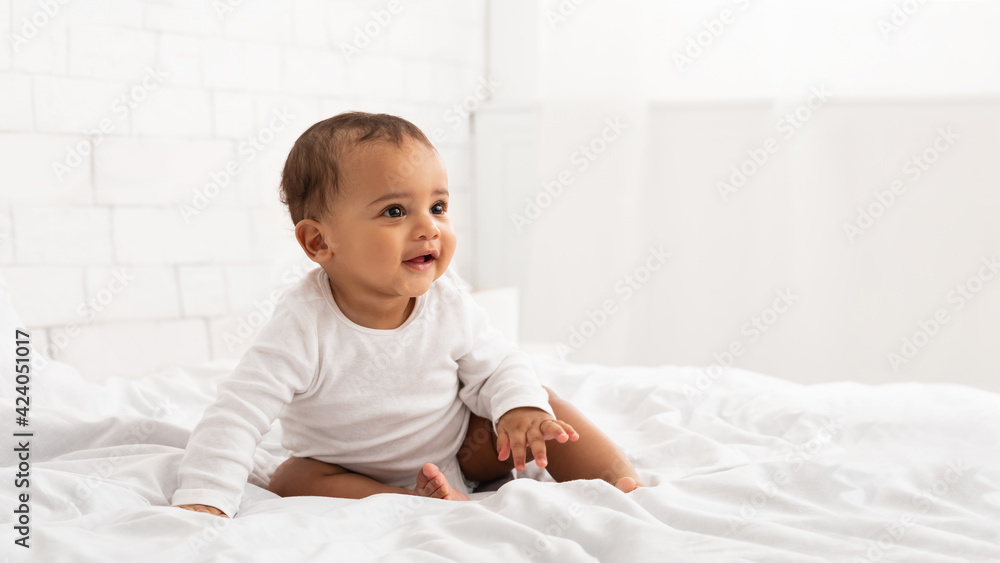 African Baby Toddler Sitting On Bed Looking Aside In Bedroom African Baby Toddler Sitting On Bed Looking Aside In Bedroom