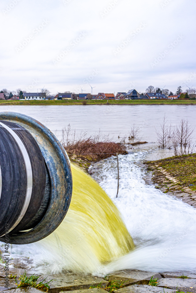 Fototapeta premium Closeup of a water pump pipe with water flowing into the Meuse river, system to control high levels of streams and prevent flooding in Geulle aan de Maas, South Limburg, the Netherlands