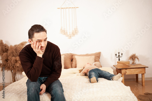 Dad can not cope with the child, a two-year-old girl lies on the bed and cries screaming hysterical. Father tired unhappy. A man is alone at home with an unruly child doesn't know how to make sleep © Valeriia