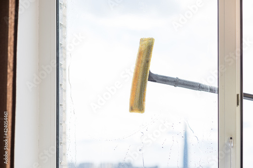 people, housework and housekeeping concept.cleaning window glass with sponge mop and foam.special brush, cleaning large open window .