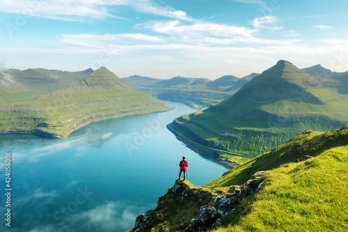Lonely tourist in red jacket looking over majestic fjords of Funningur, Eysturoy island, Faroe Islands. Landscape photography