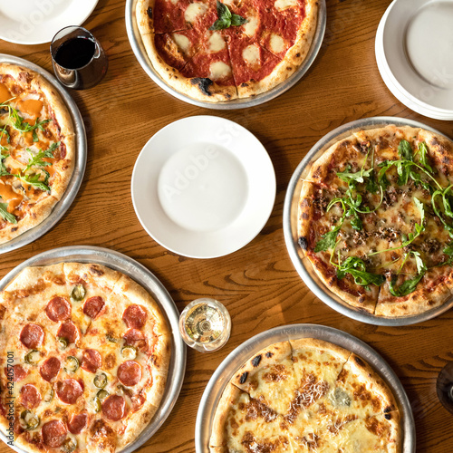 Assorted, five different pizzas on a wooden table. High angle view. Copy space for text or logo on white empty plate in center. Template for brochure or advertising banner for pizzeria or restaurant.
