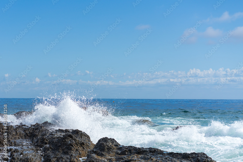 Waves crashing over black rocks in frozen motion on a warm sunny summer day. Blue and white sea colors. Rainbow Bay, Gold Coast, Queensland, Australia.