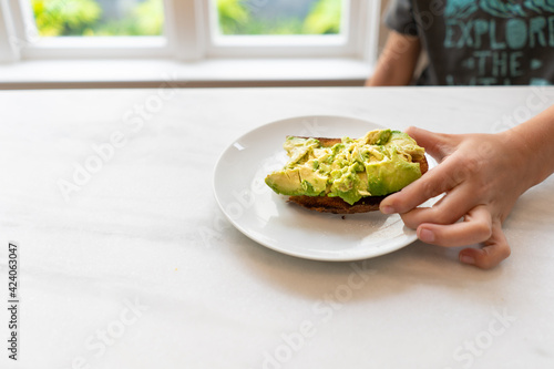 Young child eating green avocado toast for breakfast at the kitchen counter photo