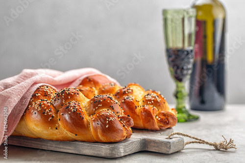 Two loaves of homemade Challah bread with pink cover, a glass of wine in background. Light grey background. Selective focus. Copy space. photo