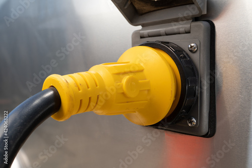 A yellow power plug and gray socket, 30 Amp, mounted in a brushed aluminum panel