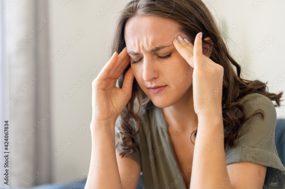 Miserable young woman touching temples sitting on the sofa at home, suffering from migraine, headache. Stressed unhappy female feels dizziness, close-up portrait Miserable young woman touching temples sitting on the sofa at home, suffering from migraine, headache. Stressed unhappy female feels dizziness, close-up portrait