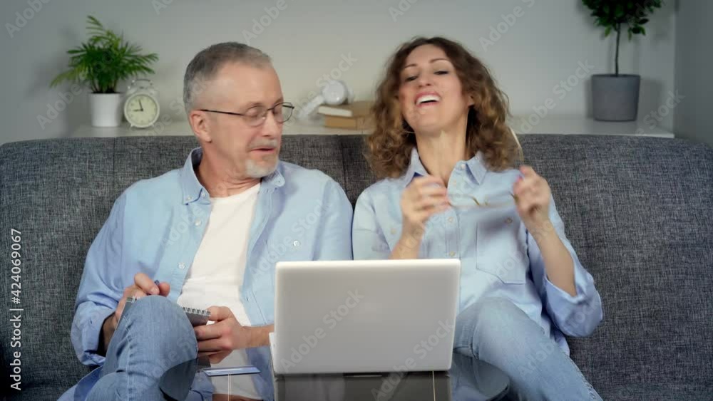 A happy middle-aged elderly couple makes online purchases on a laptop. A happy middle-aged elderly couple makes online purchases on a laptop.