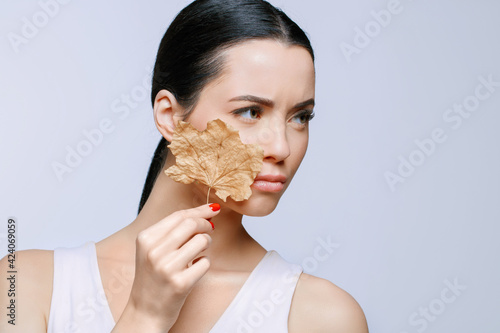 Portrait of young beautiful woman suffering the dryness on skin, holds dry leaf.