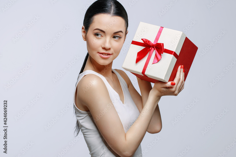 Cheerful woman holding present box in studio on gray background. Smiling beautiful young girl expressing happy emotions. Seasonal discounts and sale. Cheerful woman holding present box in studio on gray background. Smiling beautiful young girl expressing happy emotions. Seasonal discounts and sale.
