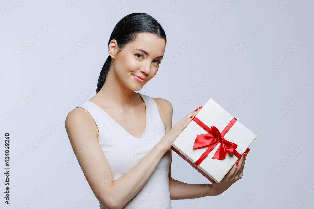 Cheerful woman holding present box in studio on gray background. Smiling beautiful young girl expressing happy emotions. Seasonal discounts and sale. Cheerful woman holding present box in studio on gray background. Smiling beautiful young girl expressing happy emotions. Seasonal discounts and sale.