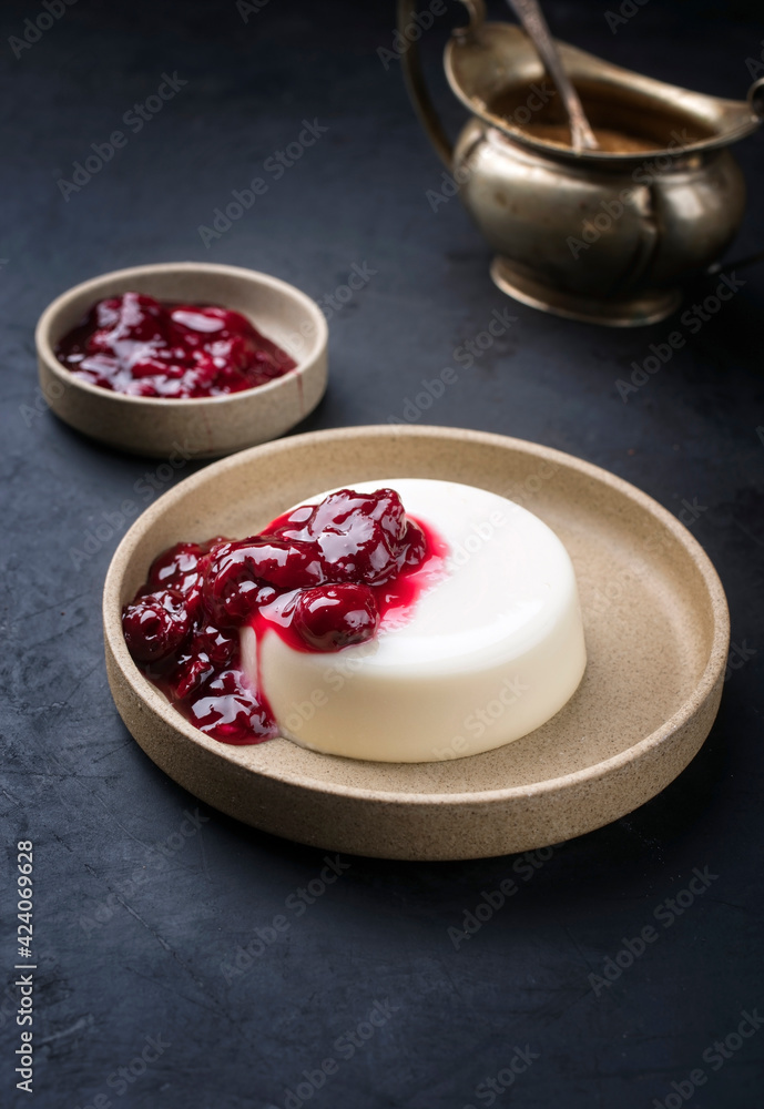 Modern style traditional blancmange almond pudding with sour cherry coulis served as close-up in a Nordic design plate on black background Modern style traditional blancmange almond pudding with sour cherry coulis served as close-up in a Nordic design plate on black background