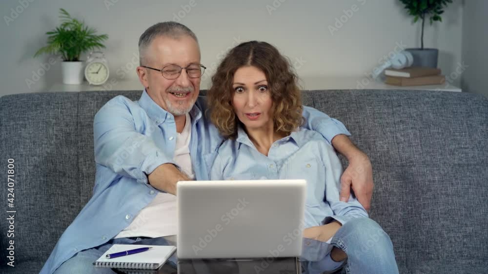A happy middle-aged couple, looking at a laptop, feels like an online winner. A happy middle-aged couple, looking at a laptop, feels like an online winner.