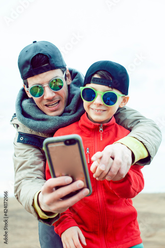 young father with his son having fun outside in spring field, happy family smiling, lifestyle people making selfie wearing sunglasses © iordani
