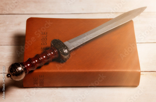 Bible with a Sword on a Bright White Wooden Table