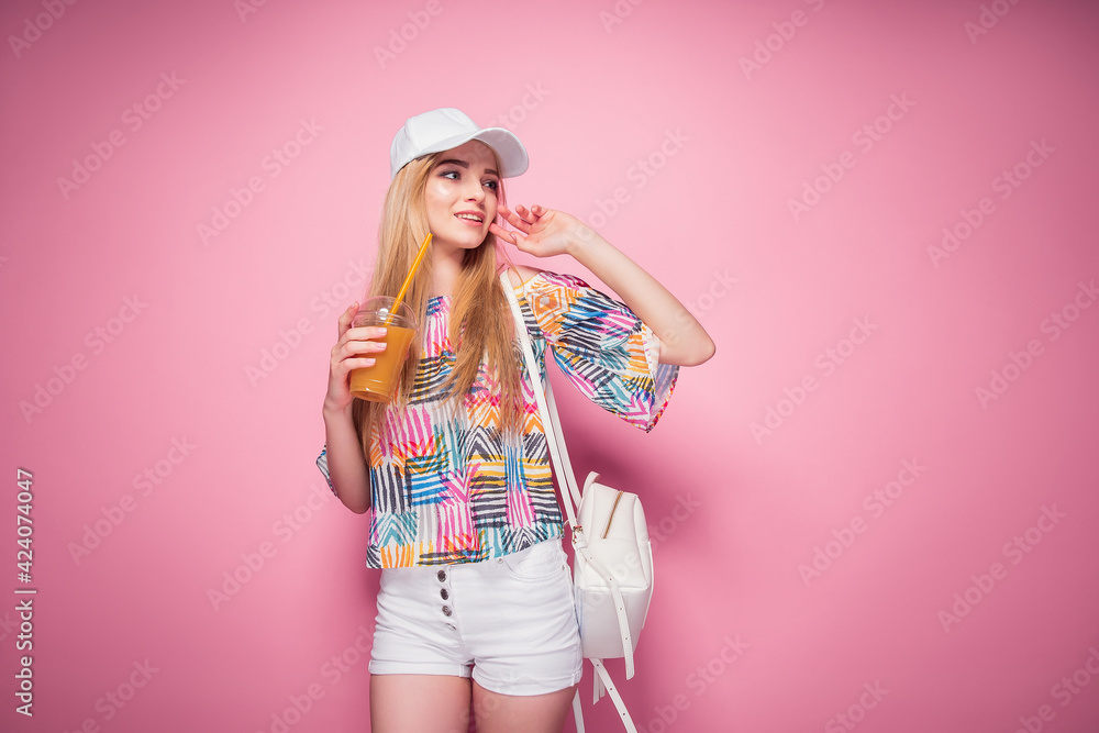 Stylish young blonde woman in cap and summer outfit holding drink in cup posing on studio background isolate Stylish young blonde woman in cap and summer outfit holding drink in cup posing on studio background isolate