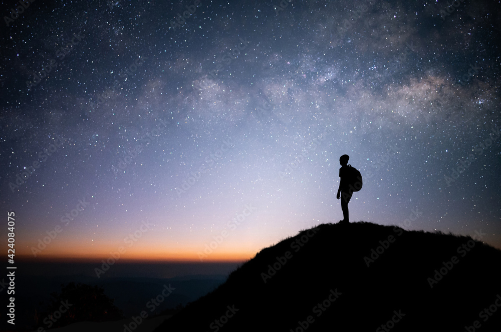 Silhouette of young traveler and backpacker standing on the top of mountains watched the star and milky way. He enjoyed traveling and was successful when he reached the summit.