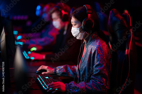 An online strategy tournament for esports players in the cyber games arena. A professional team of cyber-athletes competes with another crew, asian woman in a medical mask