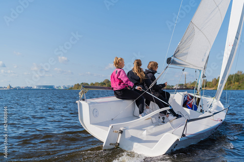 A fast, sporty, single-masted yacht with three athletes on board sails with a fair wind on a beautiful river.