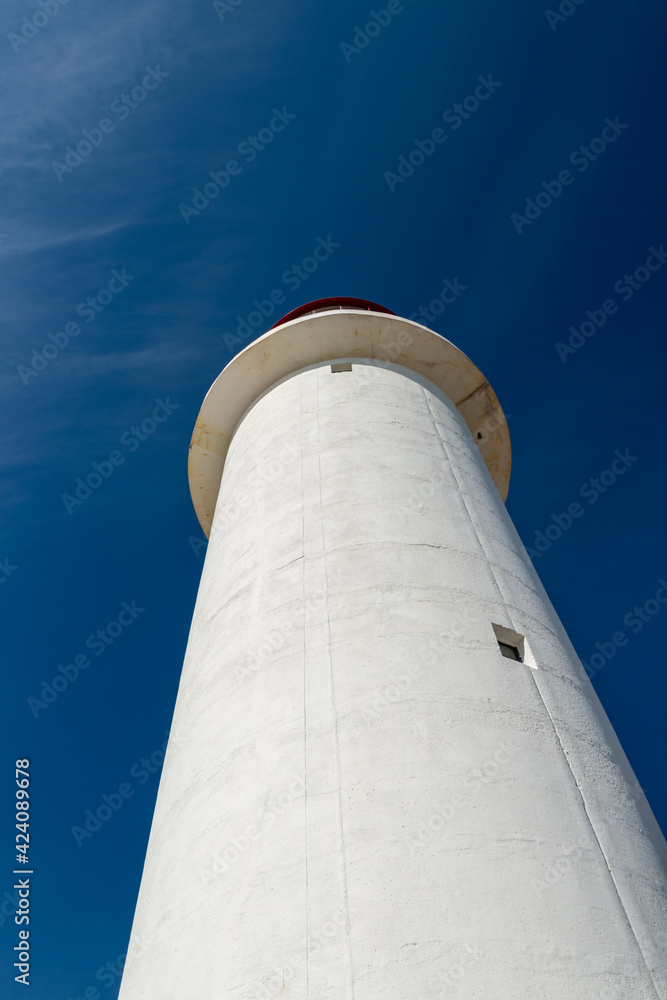 The watch room of a lighthouse.The lantern room has a large green bulb. The building is white with a red rail around the gallery deck.The background is cloudy and there's vignetting around the edges. 