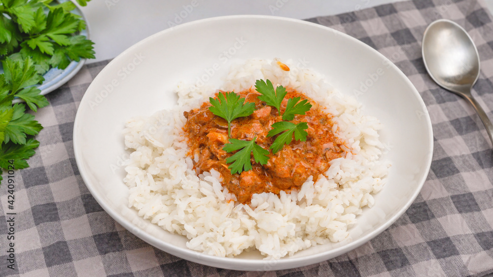 Rice with chicken meat cooked with paprika and sour cream, served with fresh parsley, close up on kitchen table Rice with chicken meat cooked with paprika and sour cream, served with fresh parsley, close up on kitchen table