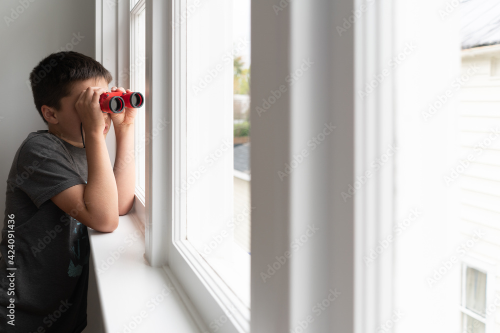 Boy looking out window of urban house with red binoculars Boy looking out window of urban house with red binoculars