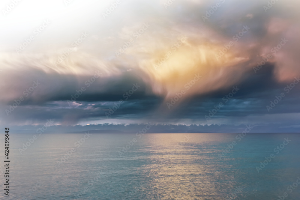 Fototapeta premium Beautiful clouds over sea. Sunlight through clouds. Beach with trees on horizon. Summer landscape. Travel background.