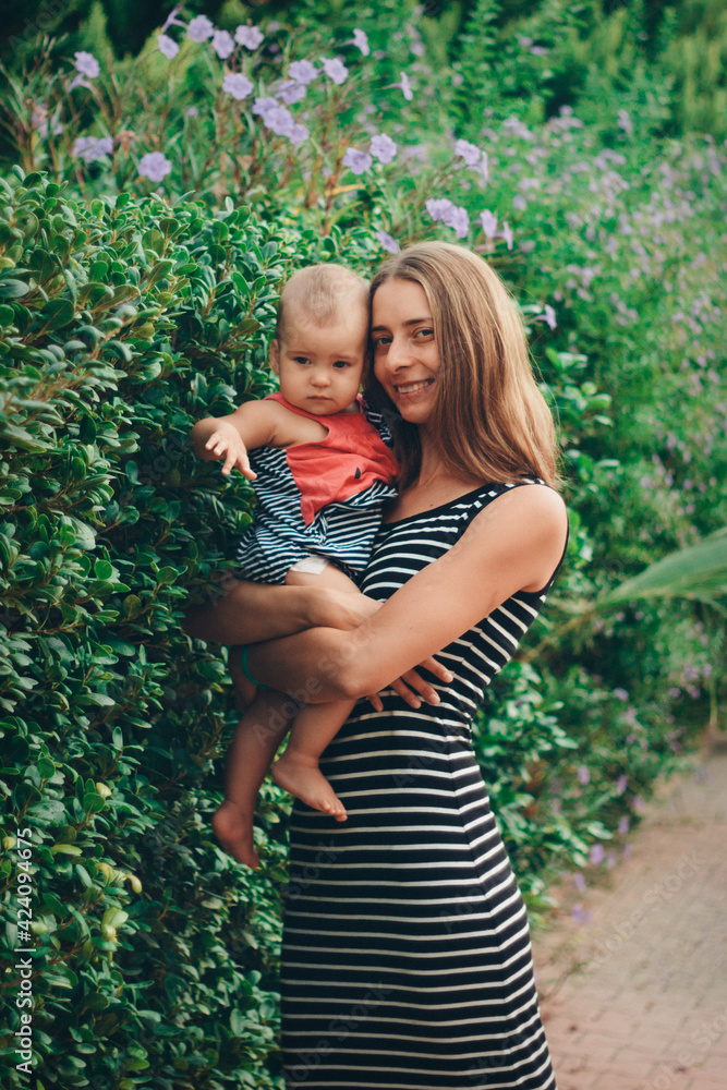 a small child sits on the mother's hands. momy's daughter is on vacation. tropical leaves. Travel to hot countries a small child sits on the mother's hands. momy's daughter is on vacation. tropical leaves. Travel to hot countries
