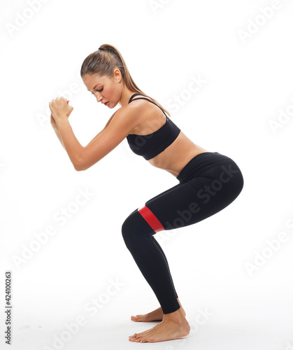 Strength and motivation. Sporty young woman squatting doing sit-ups with resistance band. Photo of woman in fashionable sportswear over white background.