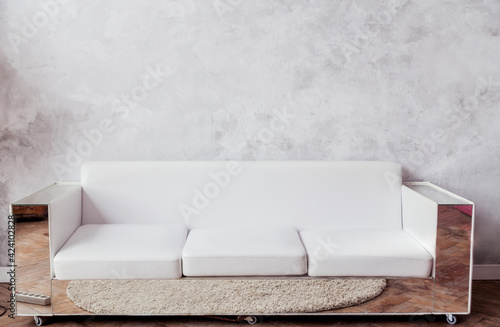 White leather sofa with mirrored frames stands against the background of a gray concrete wall