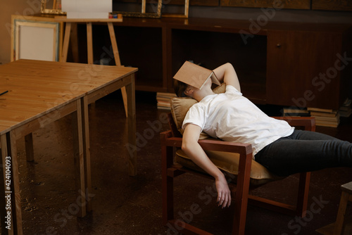 Girl in white t-shirt sleeps in dark cozy art class with book on face. Boring school lesson