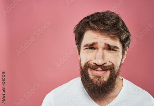 Sad man crying on a pink background in a white t-shirt cropped view