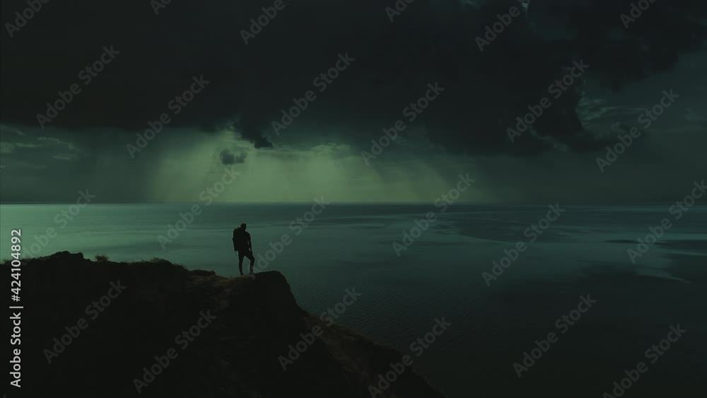 The tourist is standing on the mountain cliff on the night seascape background The tourist is standing on the mountain cliff on the night seascape background