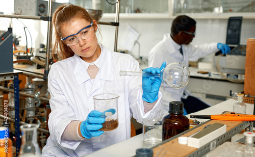 Focused woman lab technicians in glasses working with reagents and test tubes  man on background