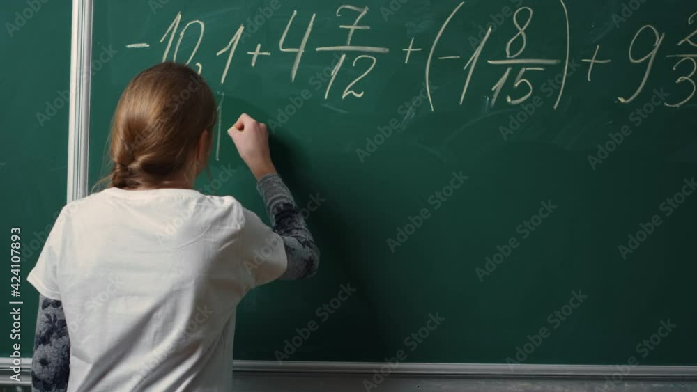 Back view of school girl doing math task on blackboard in class.Student writing Back view of school girl doing math task on blackboard in class.Student writing