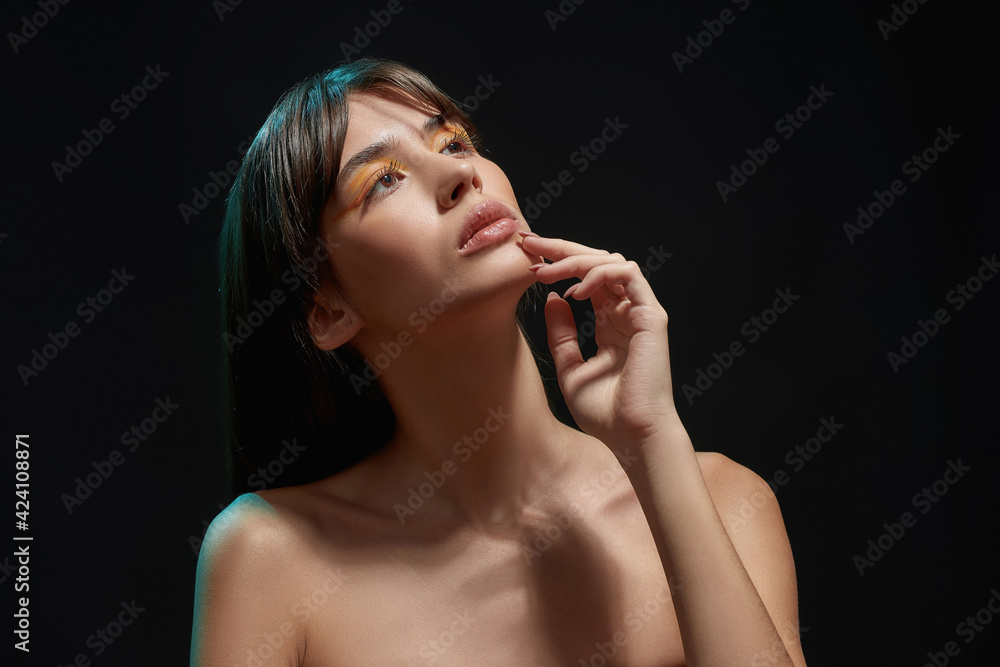 Portrait of pretty young brunette female model with colorful makeup lift her head, looking away, posing isolated over black background Portrait of pretty young brunette female model with colorful makeup lift her head, looking away, posing isolated over black background