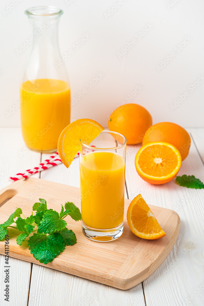 Fototapeta premium Orange juice with a glass and mint do not appear on a light background with a decanter. Side view, vertical.