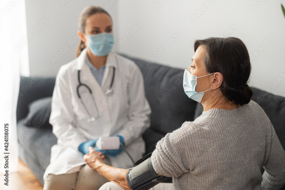 Nurse wearing mask caring about elderly female patient at home during pandemic period, the doctor monitoring blood pressure of senior female with tonometer, on-site doctor Nurse wearing mask caring about elderly female patient at home during pandemic period, the doctor monitoring blood pressure of senior female with tonometer, on-site doctor