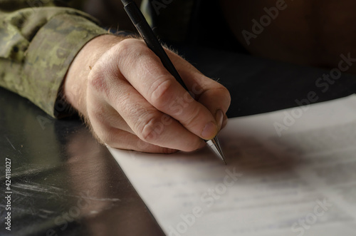 A middle-aged adult man in a green camouflage uniform signs a do