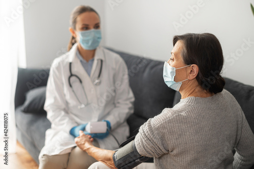 Nurse wearing mask caring about elderly female patient at home during pandemic period  the doctor monitoring blood pressure of senior female with tonometer  on-site doctor