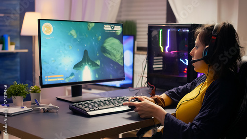 Pro player talking into microphone with other players for space shooter tournament. Gamer using wireless joystick for online championship on powerful computer late at night in gaming room