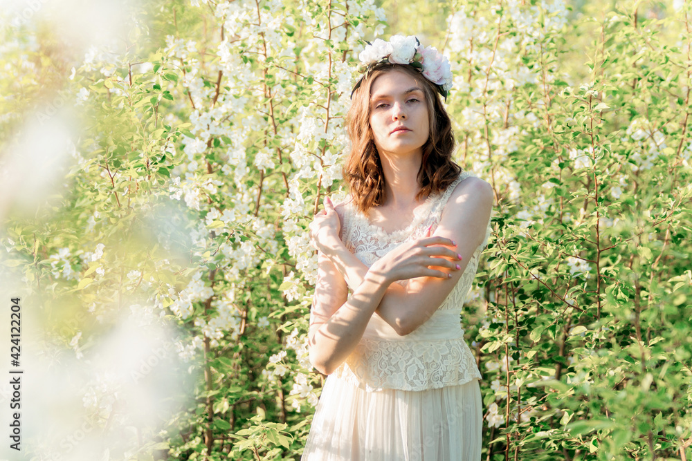 A beautiful girl in a flower wreath among the blooming apple trees