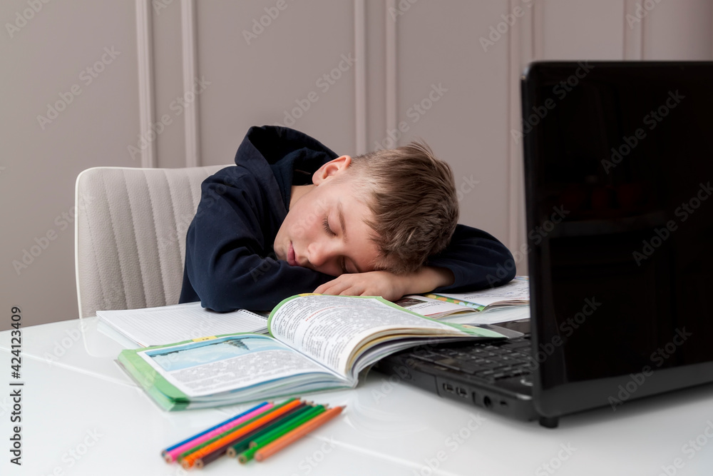 School child studying at home, tired sleep and lying on laptop while doing school homework. Distance learning online education. Back to school School child studying at home, tired sleep and lying on laptop while doing school homework. Distance learning online education. Back to school