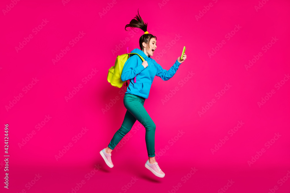 Full length photo of excited funky young lady wear blue sweater backpack looking modern device isolated pink color background