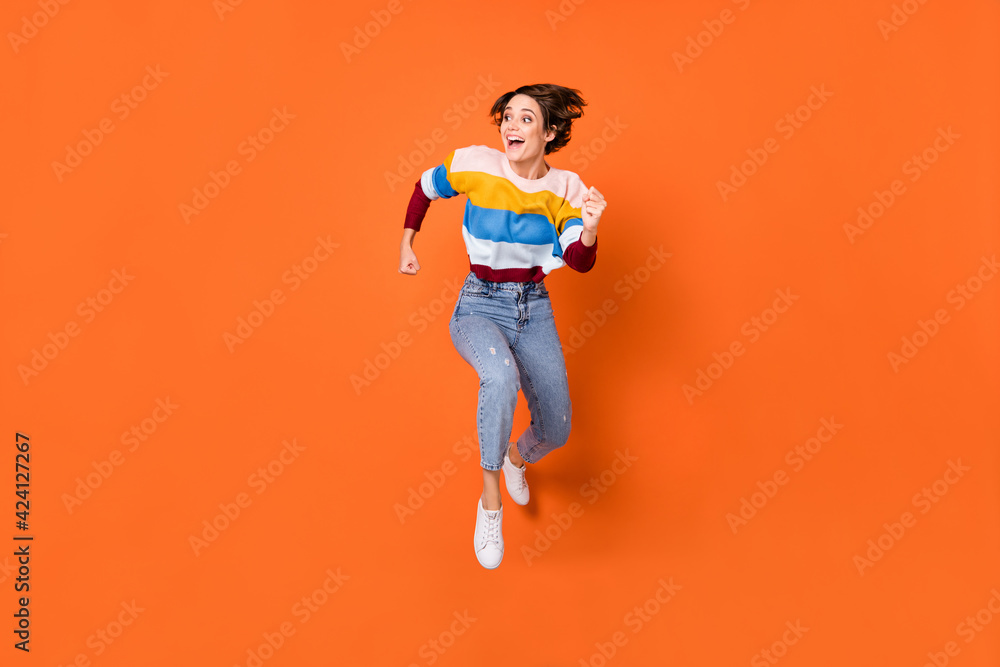 Full length body size view of attractive amazed cheerful girl jumping running having fun isolated over bright orange color background