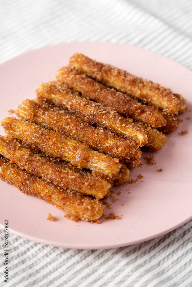 Home-baked Churro Bites on a pink plate on cloth, side view. Close-up. Home-baked Churro Bites on a pink plate on cloth, side view. Close-up.