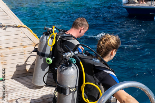 Two divers, man and woman, in swimming diving suits sit at boat before jumping at blue water and prepare diving under water in depth, view from back.