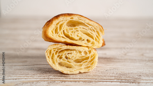 Freshly baked croissant cut in half on light wooden table. Croissant in the center of image