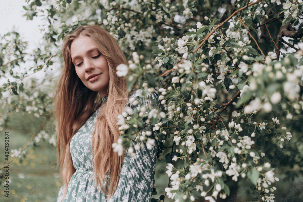 beautiful girl with brown hair in a green dress in a blooming apple orchard with white flowers beautiful girl with brown hair in a green dress in a blooming apple orchard with white flowers