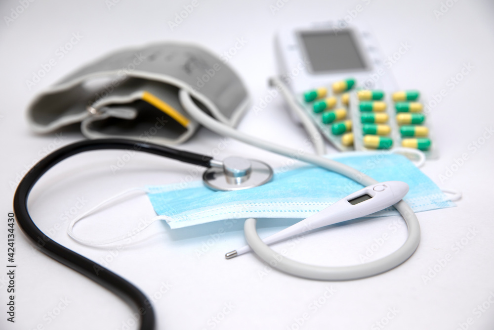 Tonometer, green tablets and a thermometer for measuring temperature. Medical mask. White background. Concept of the necessary medical items and aaparats Tonometer, green tablets and a thermometer for measuring temperature. Medical mask. White background. Concept of the necessary medical items and aaparats